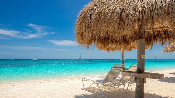 A beach with a thatched umbrella, lounge chairs, and a clear blue sea.