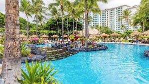 A resort pool with palm trees, lounge chairs, and a large building in the background.