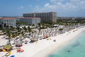A beach resort with multiple hotel buildings, a sandy beach, and numerous umbrellas. - Palm Beach Aruba | Couples Caribbean Getaway | Pool + Beach (Palm Beach)