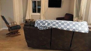 Ein Wohnzimmer mit einer Couch, einem Schaukelstuhl, einem Fernseher und einem Deckenventilator.