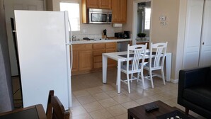 A compact kitchen with wooden cabinets, a microwave, and a refrigerator. There is a dining area with a table and chairs.