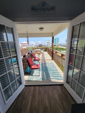 Blick von einer überdachten Terrasse mit einem Schild 'Welcome to the Beach', Holzwertungen und roten Stühlen.