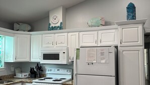 Una cocina con armarios blancos, estufa, horno microondas y refrigerador.
