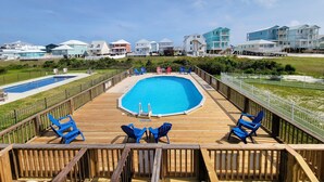 Una terraza de madera con piscina, sillas azules y vistas a casas de playa.