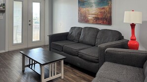 Een woonkamer met een grijze bank, een rode lamp en een plafondventilator.