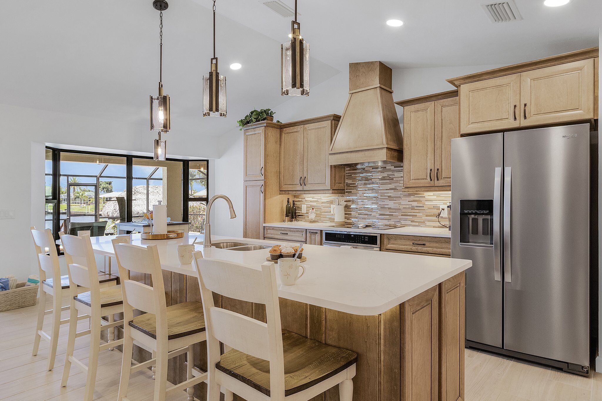 A modern kitchen with a central island, stainless steel appliances, wooden cabinets, and pendant lighting.