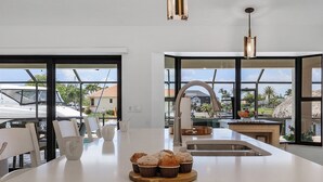 A modern kitchen with a large island, a sink, and a view of the outdoors. - Amazing water views, heated pool & spa, Tiki & kayaks -Villa SeaOarNo - Roelens Vacations (Cape Coral)