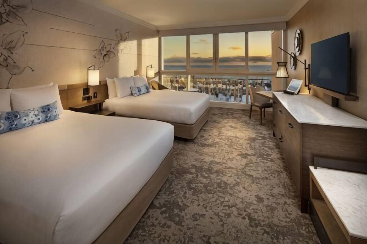 A hotel room with two beds, a desk, a chair, a TV, and a city view.