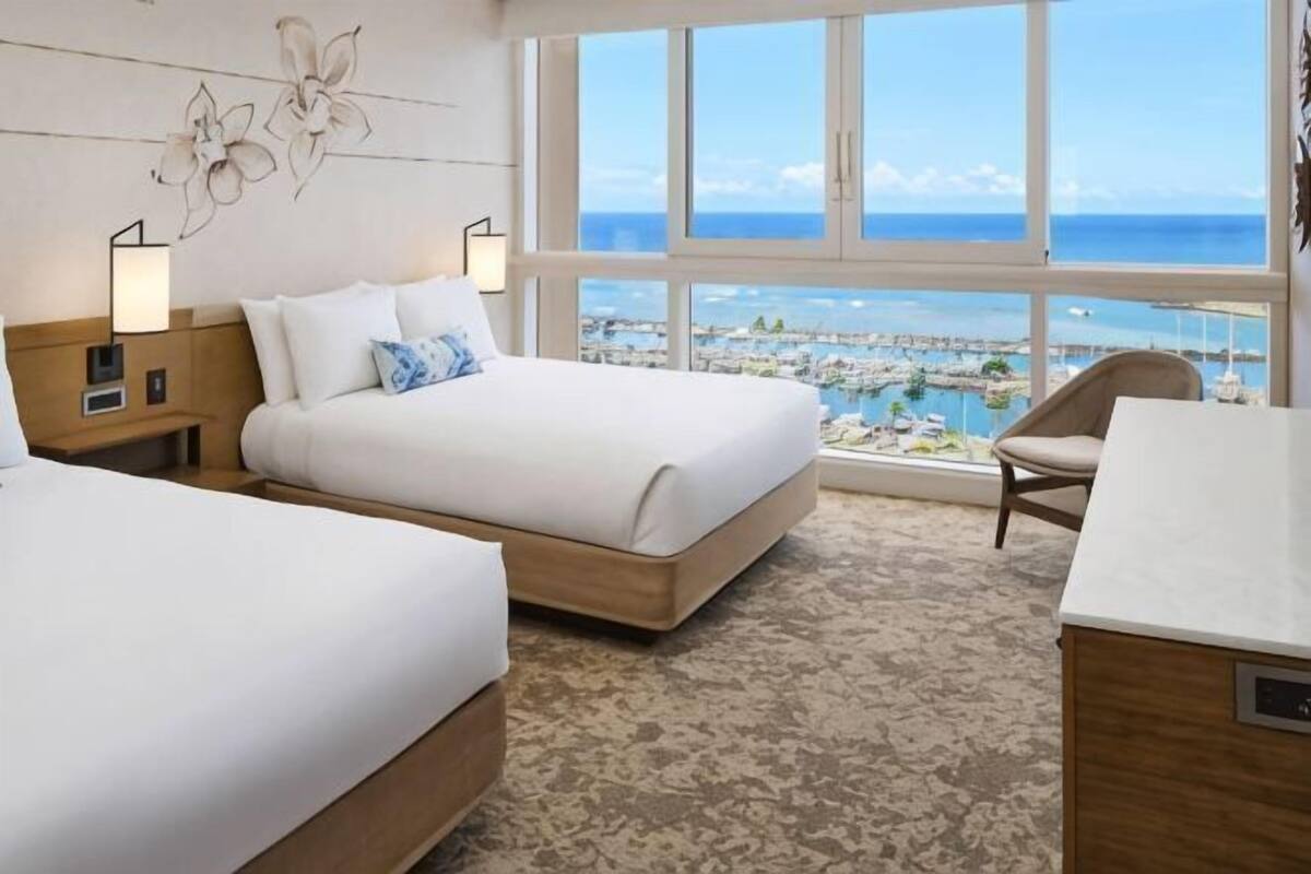 A hotel room with two beds, a view of the beach, and a chair by the window.