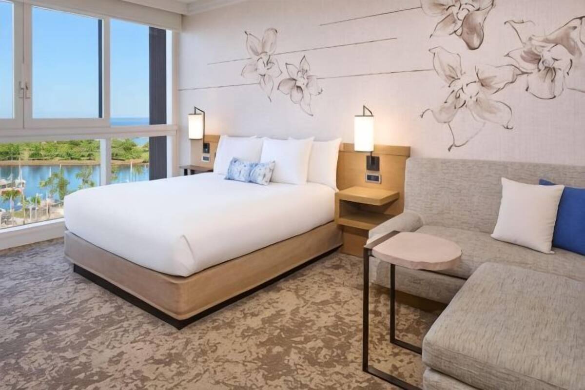 A hotel room with a large bed, a sofa, a small table, and a view of a body of water.