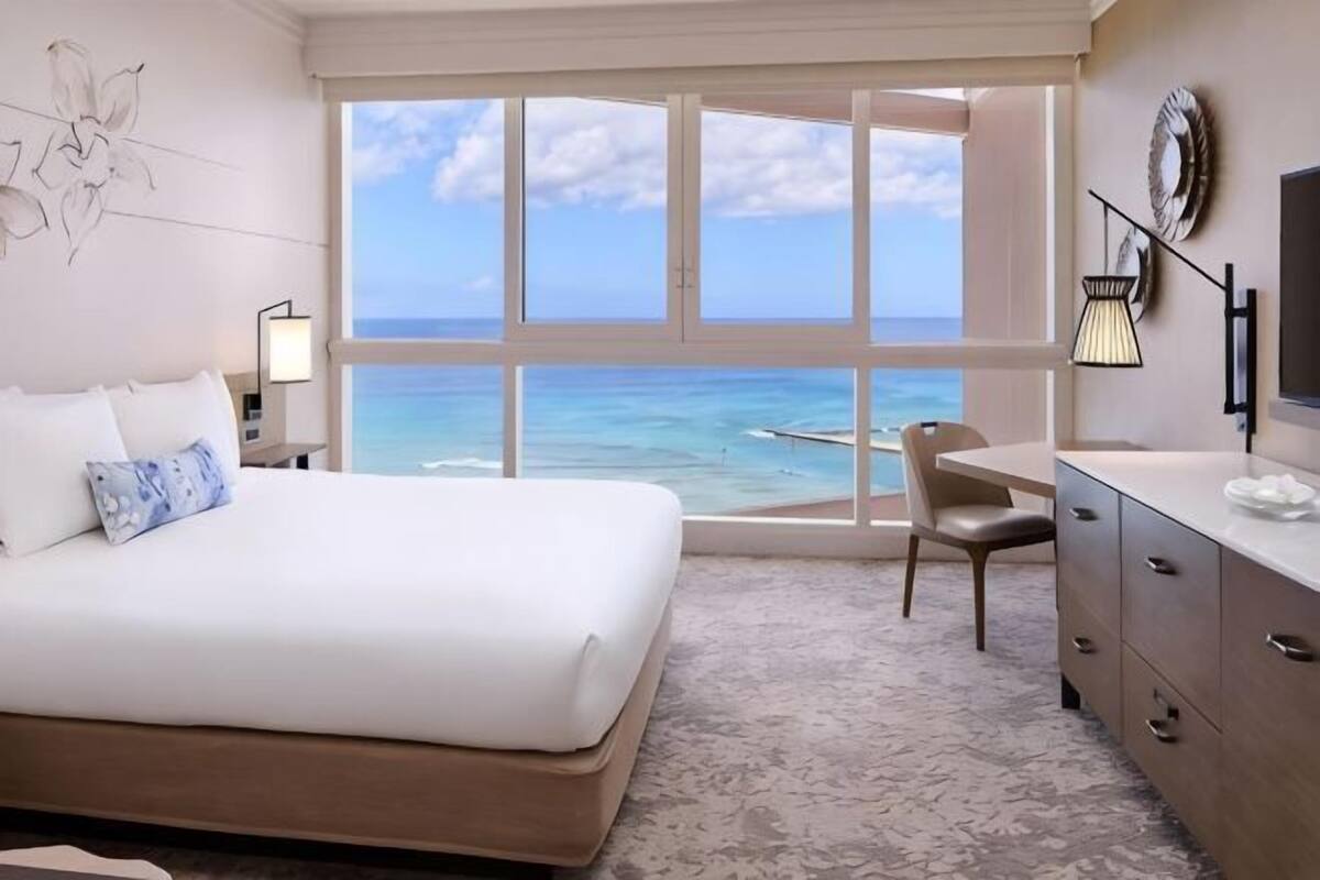 A hotel room with a large bed, a desk, a chair, and a view of the ocean.