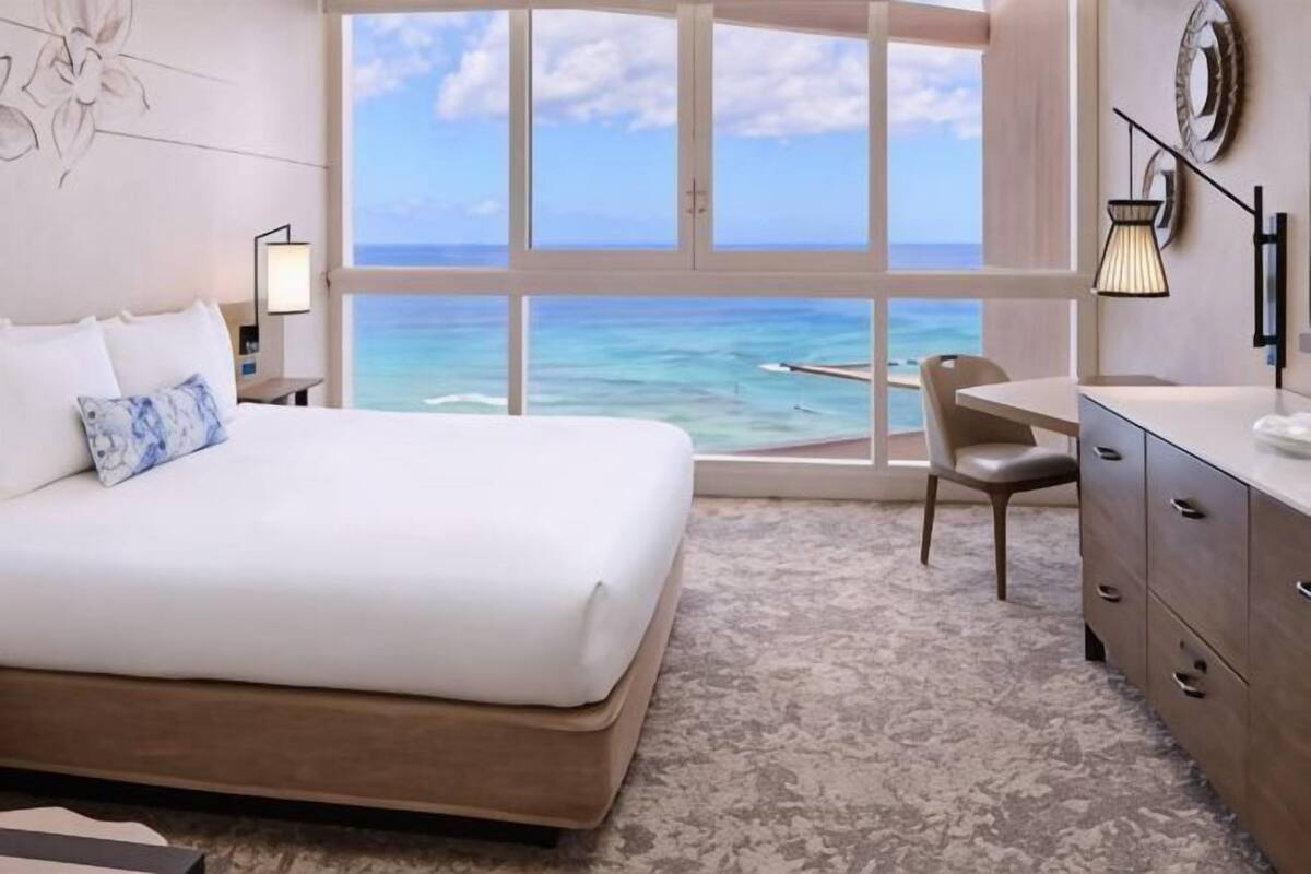 A bedroom with a large bed, a desk, and a view of the ocean.