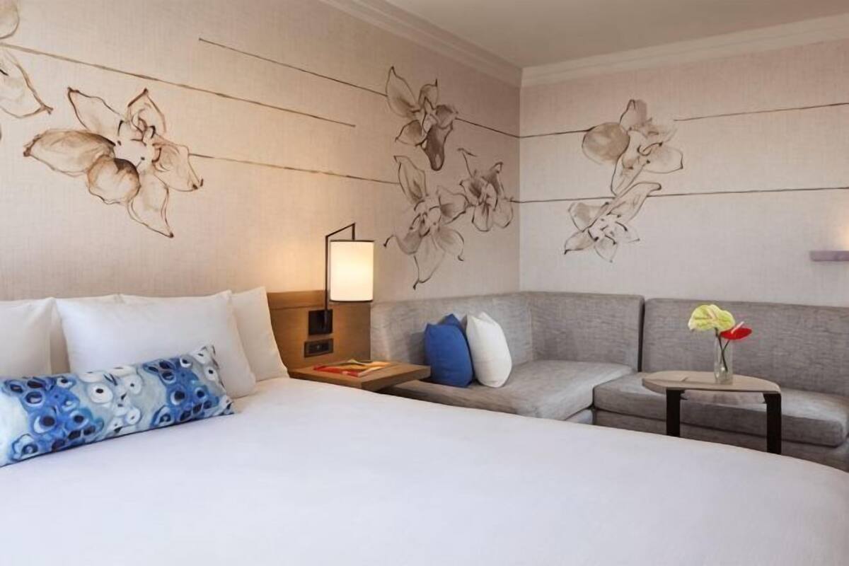 A hotel room with a large bed, a sofa, a small table with a vase, and a wall with floral artwork.