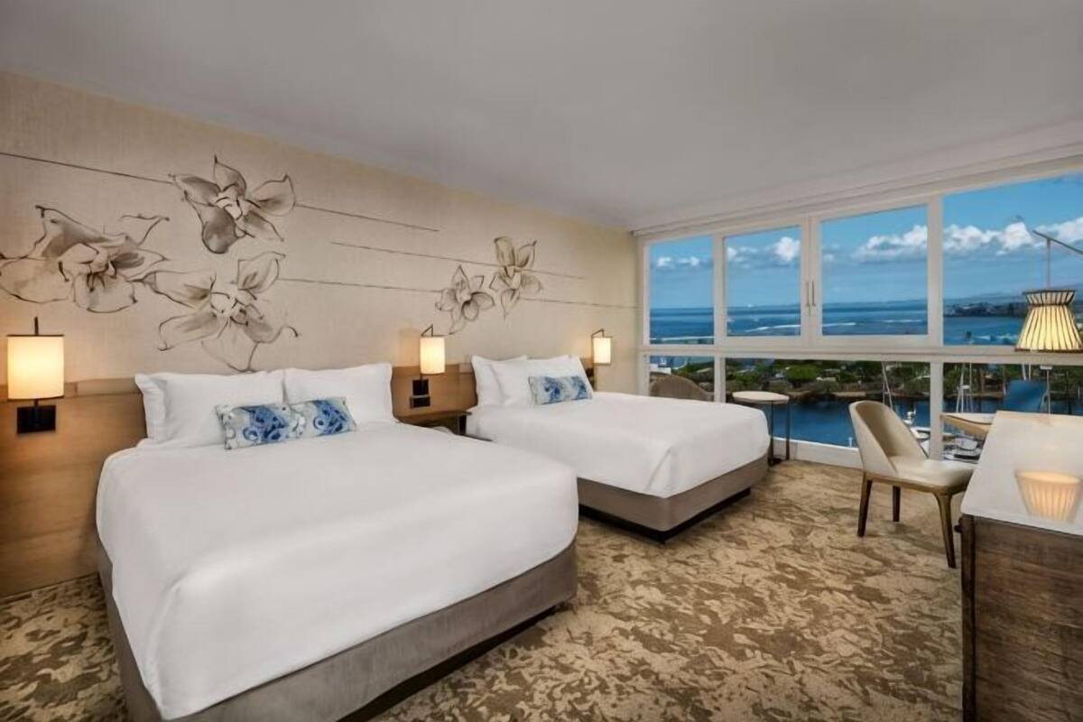 A hotel room with two beds, a view of the ocean, and a balcony with a chair.