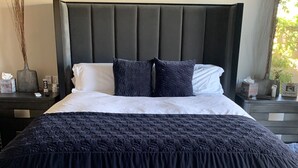 A neatly made bed with a dark headboard and pillows, a bedside table with a vase and a box, and a window with curtains. - Indian Wells Exclusive Home on Golf Course (Indian Wells)