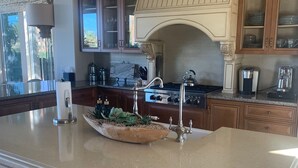 A kitchen with a large island, wooden cabinets, a stove, and a decorative chandelier. - Indian Wells Exclusive Home on Golf Course (Indian Wells)
