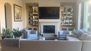 A modern living room with a large sectional sofa, a fireplace, and built-in bookshelves. - Indian Wells Exclusive Home on Golf Course (Indian Wells)