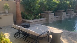 A patio area with a table and chairs, a small fountain, and a pool. - Indian Wells Exclusive Home on Golf Course (Indian Wells)