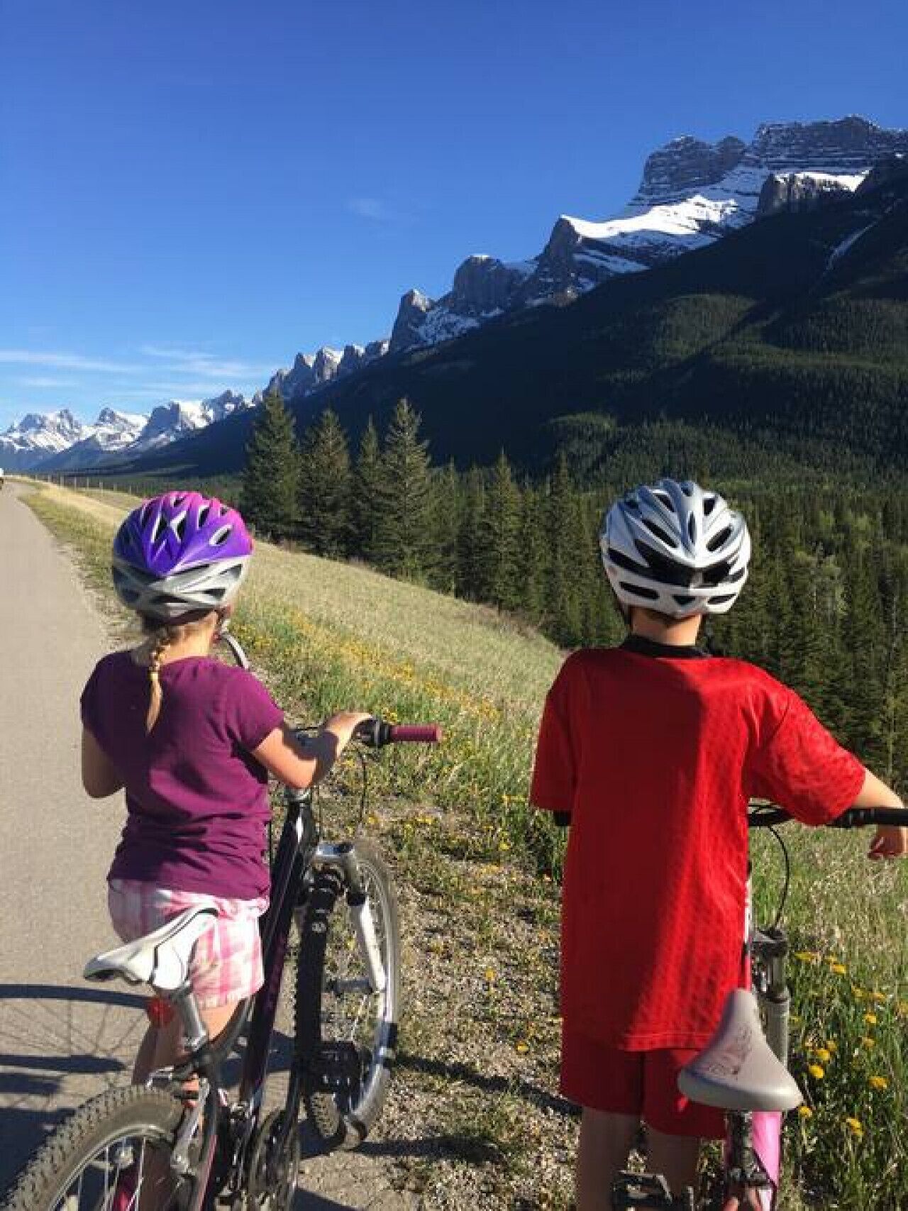 Dos niños en bicicleta sobre un camino pavimentado con montañas al fondo.