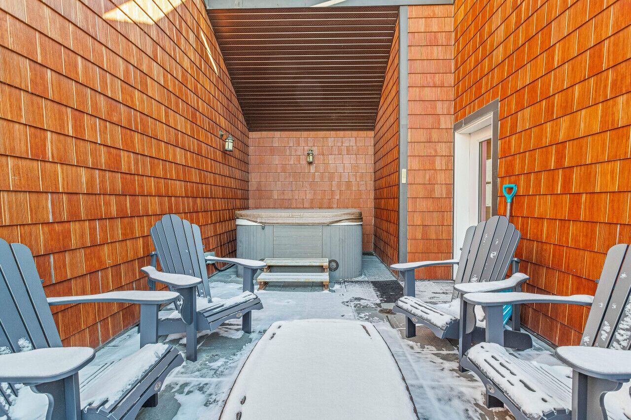 A heated outdoor area with Adirondack chairs and a hot tub, surrounded by wooden walls.