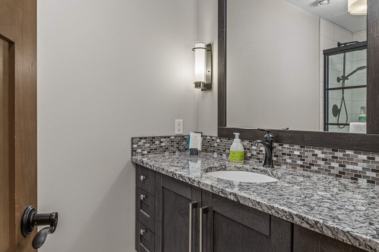 A bathroom with a marble countertop, a sink, a mirror, and a shower area.