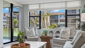 Ein modernes Wohnzimmer mit großem Fenster, einer Sofagarnitur, einem Couchtisch und einem Korbstuhl mit Pflanzen.
