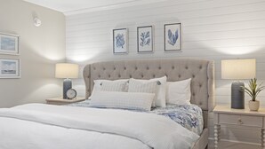 Ein Schlafzimmer mit einer karotierten Kopfteile, einem Bett mit weißer Bettwäsche, zwei Nachttischen mit Lampen und gerahmten botanischen Drucken an der Wand.