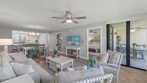 Ein geräumiges Wohnzimmer mit einer Couch, einem Couchtisch und Sesseln. Es gibt eine Essecke mit Tisch und Stühlen, und im Hintergrund eine Küche.