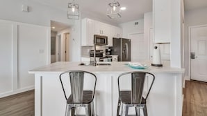 A modern kitchen with white cabinets, stainless steel appliances, and a central island with two bar-style chairs.