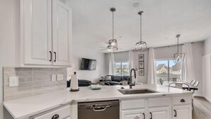 A modern kitchen with white cabinetry, a dishwasher, and pendant lighting.