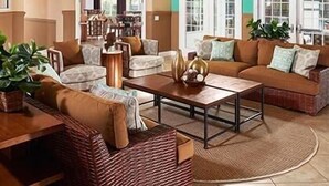 A spacious living room with a large sofa set, a coffee table, and a dining area with chairs. There are potted plants and a decorative wall piece. - BELLA VIDA (891MB) - AMAZING 5BR 4BA HOME*POOL&SPA*GATED RESORT (Kissimmee)