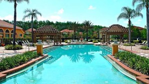 A swimming pool with lounge chairs and palm trees, surrounded by buildings with arched windows. - BELLA VIDA (891MB) - AMAZING 5BR 4BA HOME*POOL&SPA*GATED RESORT (Kissimmee)