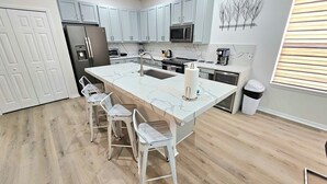 A modern kitchen with light blue cabinets, a large island with bar stools, and a stainless steel refrigerator. - BELLA VIDA (891MB) - AMAZING 5BR 4BA HOME*POOL&SPA*GATED RESORT (Kissimmee)