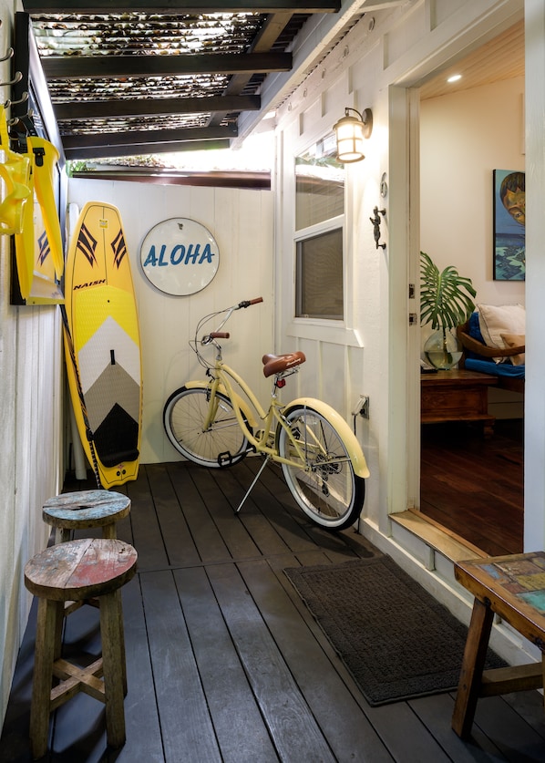 A wooden deck with a bicycle, a surfboard, and a small stool.