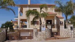 A two-story building with a stone entrance gate, a balcony, and a flag. - Villa Omega Kefalonia (Karavados)