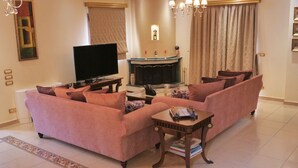 A living room with a sofa set, a flat-screen TV, a fireplace, and a chandelier. - Villa Omega Kefalonia (Karavados)