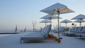 A beachside lounge area with sun loungers and umbrellas, a pool, and a clear view of the sea. - Liwa Hotel Abu Dhabi (Mezaira'a)