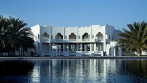 A large, white building with multiple balconies and arched windows, surrounded by a pool and palm trees. - Liwa Hotel Abu Dhabi (Mezaira'a)