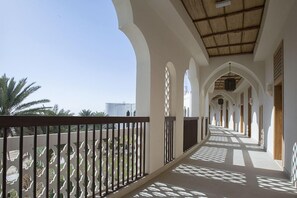 Un couloir orné d’arches et doté d’une balustrade décorative, qui mène à un bâtiment au toit de chaume.