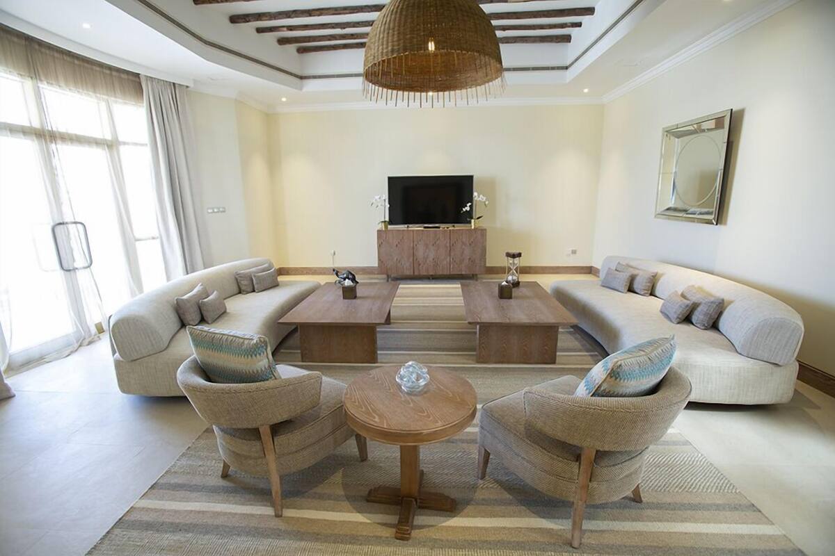 Een ruime woonkamer met een grote zithoek, twee houten salontafels en een televisie op een houten kast.
