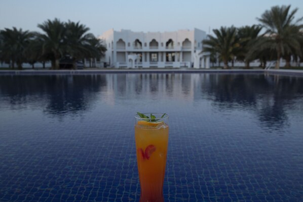 A pool with a drink in the foreground and a building in the background.