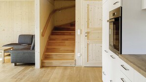 A modern interior with a wooden staircase, a grey sofa, and a kitchen area with white cabinets and a built-in oven. - großes Ferienhaus in Altaussee (Altaussee)