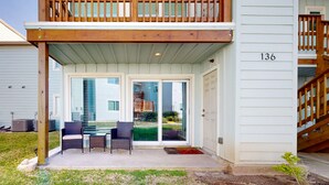 A two-story house with a balcony, a covered patio with chairs, and a sliding glass door. - Golf Cart Included, First Floor, Near Marina, Pet Friendly (Port Aransas)