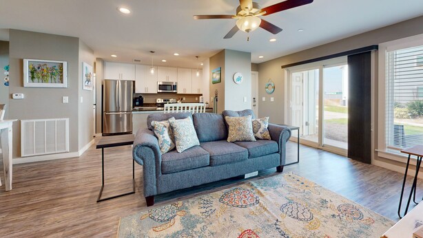 A modern living room with a grey sofa, a patterned rug, and a ceiling fan. - Golf Cart Included, First Floor, Near Marina, Pet Friendly (Port Aransas)