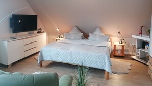 A bedroom with a bed, bedside lamps, a TV, a desk, and a shelf with items.