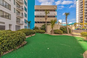 A courtyard with artificial green turf, palm trees, and a building with balconies.