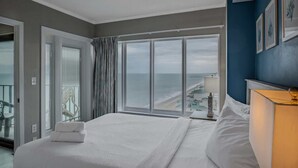 Habitación de hotel con una cama grande, vista al océano y un balcón con barandilla.