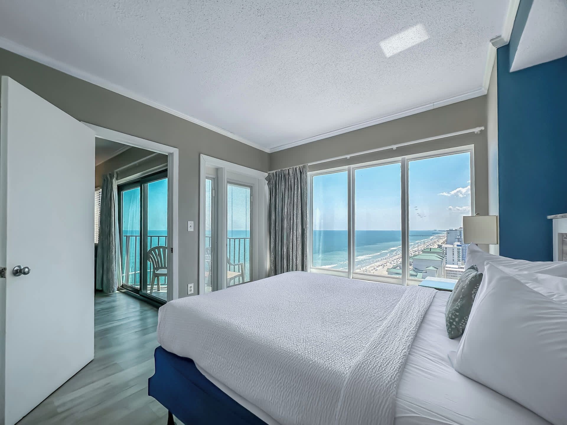 A hotel room with a large bed, a view of the ocean, and a balcony with a chair.