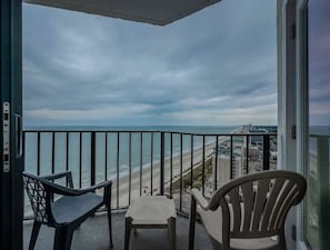Un balcón con vista a la playa y al paisaje urbano, dos sillas y una mesita.