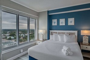 A hotel room with a large window, a bed with white linens, and three framed pictures on the wall. - Palace 2113 (Myrtle Beach)